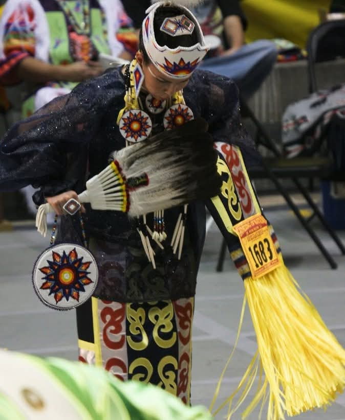 A dancer in regalia holding a feather fan at a community gathering