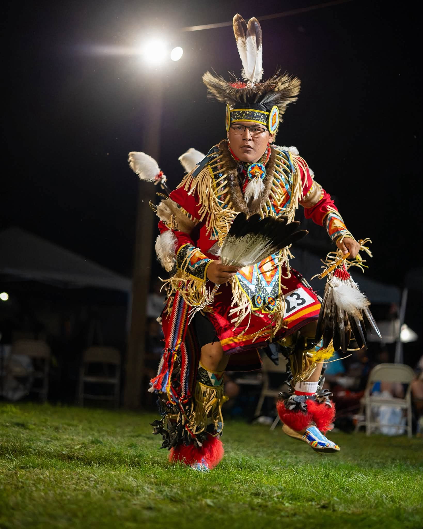 A dancer in colorful regalia performing outdoors at night